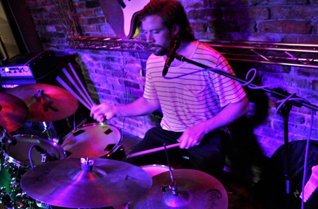 A man playing drums in front of purple lights.
