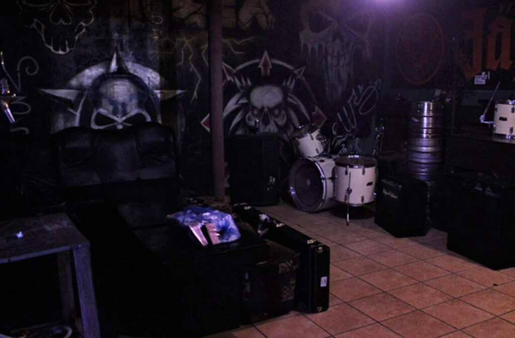 A room with a black leather couch and a large skull painted on the wall.