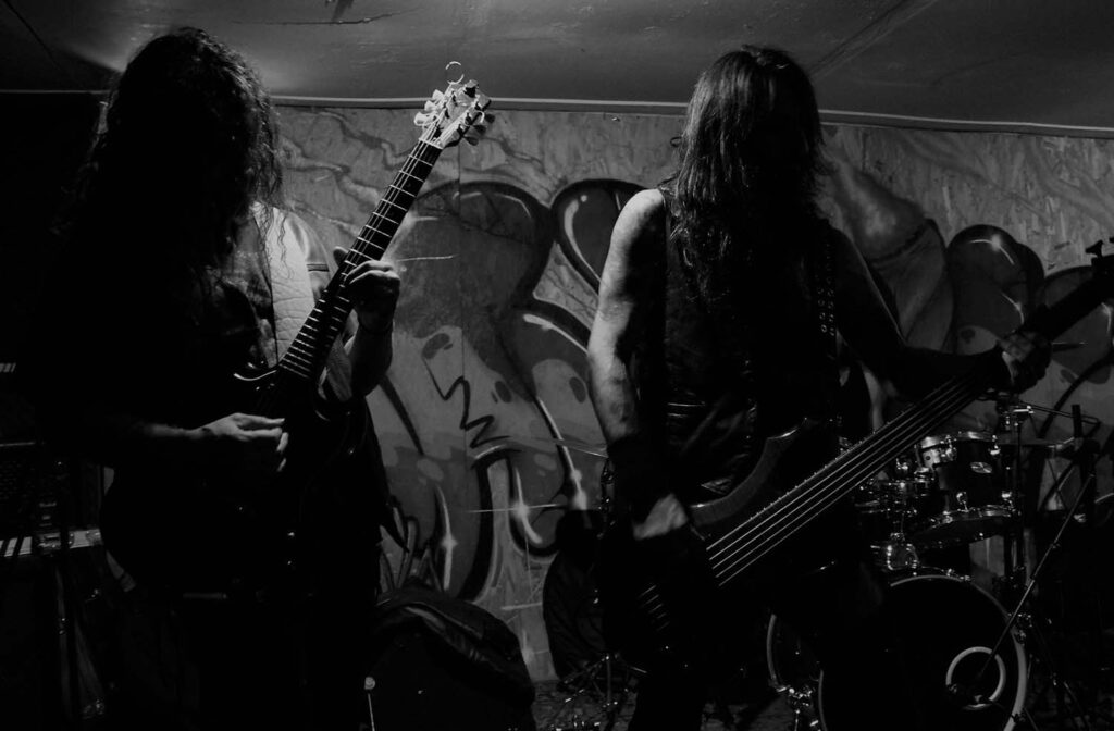 Two people playing guitars in front of a wall.