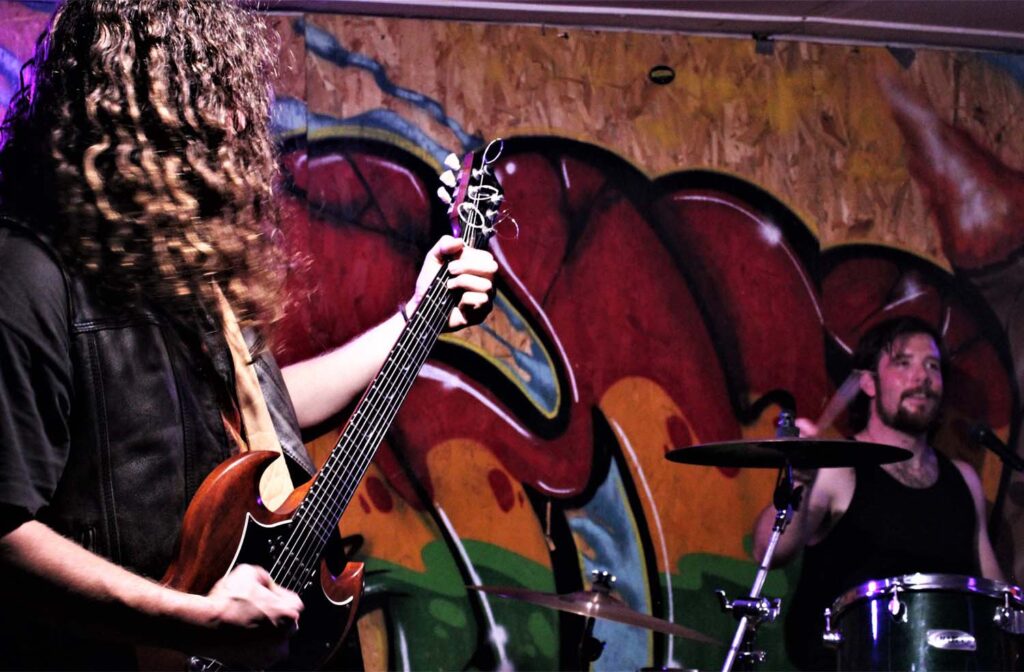 A person playing guitar in front of a wall with graffiti.
