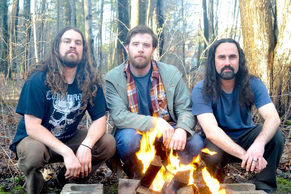 Three men sitting in front of a fire.