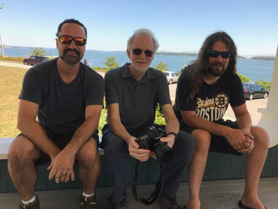 Three men sitting on a bench with a camera.