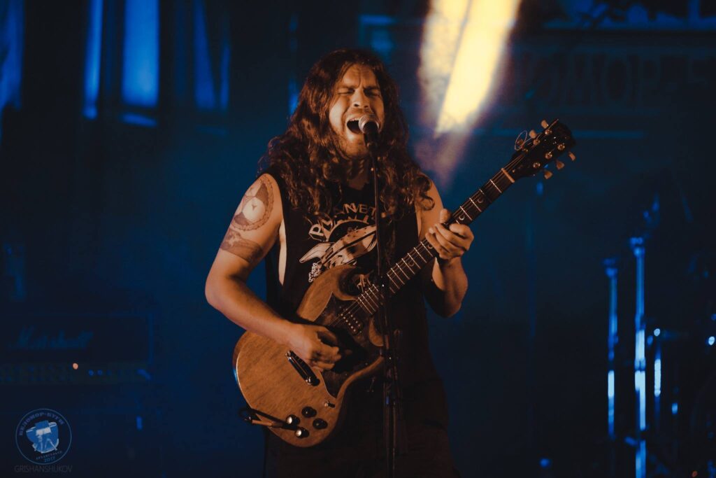 A person with long hair and tattoos playing an electric guitar.